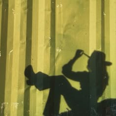 a shadow of a man holding a baseball bat in front of a yellow wall with vertical stripes