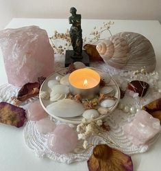 a candle sits on a plate surrounded by sea shells and other seashells, along with a small figurine