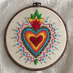 a colorful heart is in the middle of a cross stitch pattern on a white background