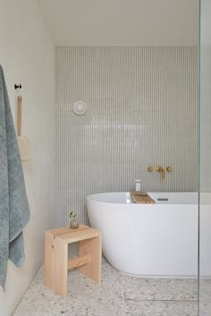 a white bath tub sitting next to a wooden stool in a bathroom under a window