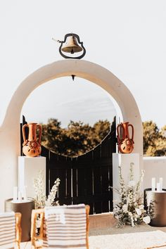 an arch with two vases on it and some flowers in the foreground,