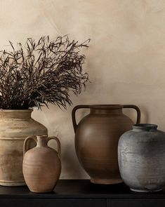 three vases sitting on top of a black table next to a plant in a vase