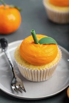 a cupcake with an orange frosting and a green leaf on top sits on a plate