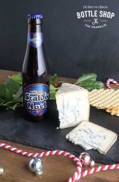 a bottle of beer next to some crackers on a black board with christmas decorations