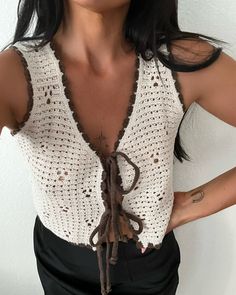 a woman with her hands on her hips wearing a crochet top and black pants