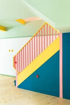 an empty room with blue, yellow and pink painted stairs next to a wooden floor