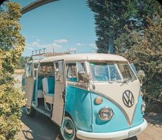 a blue and white vw bus parked next to trees