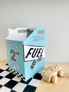 a cardboard box that is sitting on top of a checkered tablecloth with two wooden toy cars in front of it