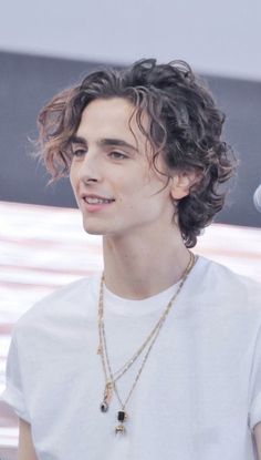 a young man with curly hair wearing a white t - shirt and holding a microphone