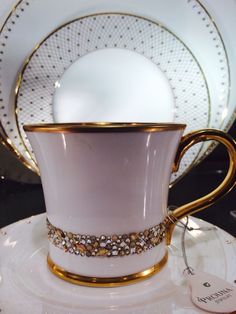 a white and gold coffee cup sitting on top of a plate next to a stack of plates