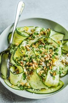 a white bowl filled with cucumbers and nuts on top of a gray table