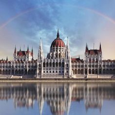 a large building that has a rainbow in the sky above it and water below it