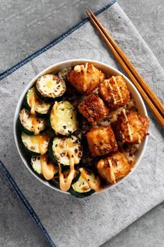 a white bowl filled with food next to chopsticks on top of a table