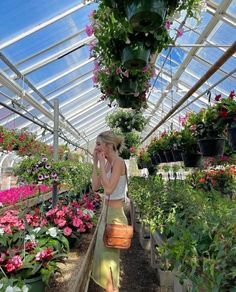 a woman is talking on her cell phone while walking through a greenhouse filled with flowers