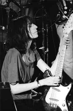 a black and white photo of a woman playing an electric guitar with another person in the background