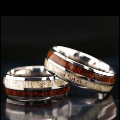 two wedding rings with antler wood inlays on top of each other, sitting on a reflective surface