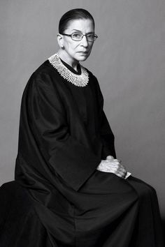 an older woman in a black gown sitting on a chair