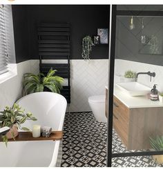 a white bath tub sitting next to a toilet in a bathroom under a window filled with plants