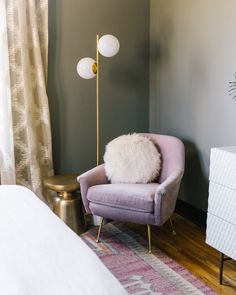 a purple chair with a white pillow on top of it in front of a bed