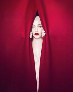 a woman is hiding behind a red curtain with her head in the middle of it