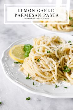 two plates of spaghetti with lemon wedges and parmesan cheese on the side