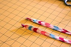 two pink and blue striped straws sitting on top of a cutting board next to scissors