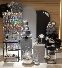 a table topped with lots of silver and black desserts next to balloons in the background