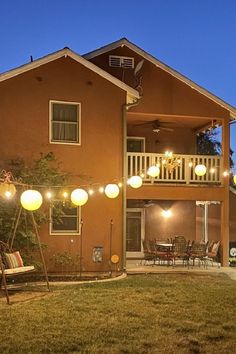 an outdoor patio with lights strung from the ceiling and furniture on the lawn outside at night