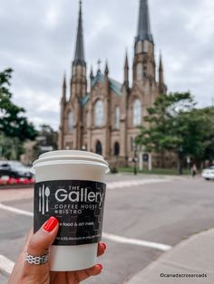 a woman holding up a cup of coffee in front of a church with spires