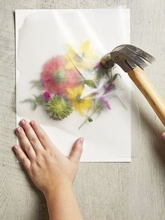 a person holding a paintbrush over a flower on a piece of paper with flowers painted on it