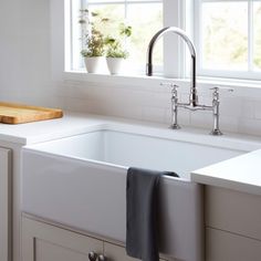 a white kitchen sink sitting under a window next to a cutting board and potted plant