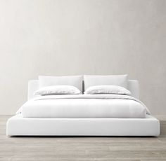 a bed with white sheets and pillows on top of it in a room that has wood floors