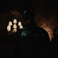 the dark knight is standing in front of a chandelier with lights behind him