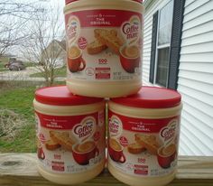 three jars of coffee creamer sitting on top of a wooden table in front of a house