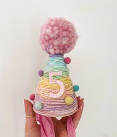 a hand holding up a small birthday hat made out of yarn and pom poms