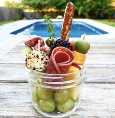 a glass jar filled with assorted fruits and snacks next to an outdoor swimming pool