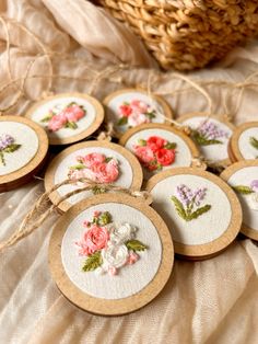 embroidered flowers are displayed on small wooden coasters in front of a wicker basket