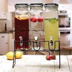 three different types of drinks in glass bottles on a table next to lemons and strawberries