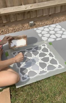 a woman is painting on the ground with white and gray tiles in front of her