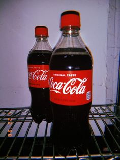 two bottles of coca - cola sitting on top of an oven rack