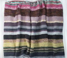 a multicolored knitted blanket hanging on a white door with the curtain open