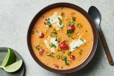 a bowl of soup with tomatoes, cheese and green garnish next to a spoon