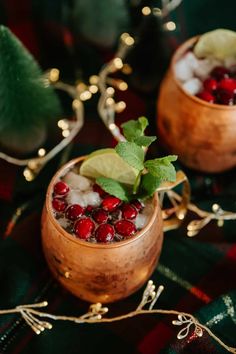 two copper mugs filled with drinks and garnished with cranberries, mint leaves and lime