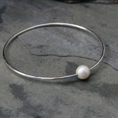 Luminous white freshwater pearl slides freely around this sterling silver bangle. The bangle has been hand formed, lightly hammered, and polished for a lovely finish. Available in 3 sizes: Small 7.25 inches around x 2.25 inches across Medium 8 inches around x 2.5 inches across Large 8.75 inches around x 2.75 inches across Beautiful worn as a single adornment, or stacked with your favorite bangles. For more Pearl Bangles: https://www.etsy.com/shop/KiraFerrer/search?search_query=pearl+bangles&view Pearl Bangles, Heart Bangle Bracelet, White Pearl Bracelet, Stackable Bangles, Birthday Bracelet, Pearl Bangle, The Bangles, Sterling Silver Bangle, White Freshwater Pearl