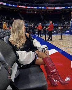 a woman sitting on top of a chair in front of a basketball court while wearing red boots