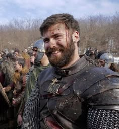 a man in armor is smiling at the camera with other people behind him, all dressed up and ready for battle