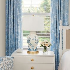 a blue and white vase sitting on top of a dresser next to a window with curtains