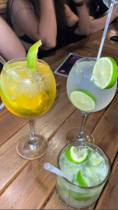 three different types of drinks sitting on a wooden table next to each other with limes in them