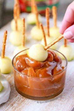 someone dipping something into a small glass dish with pretzels on top and other appetizers in the background