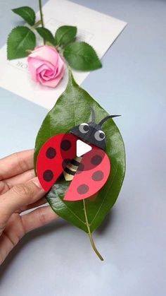 a ladybug brooch sitting on top of a green leaf next to a pink rose